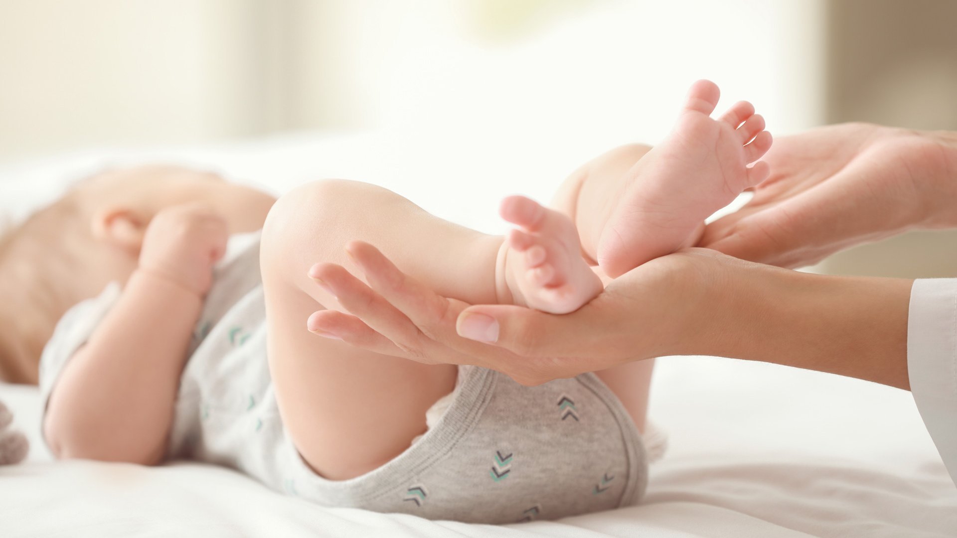 Ein Baby liegt auf einer Wickelkommode. Die Mutter hält die Füße in der Hand.