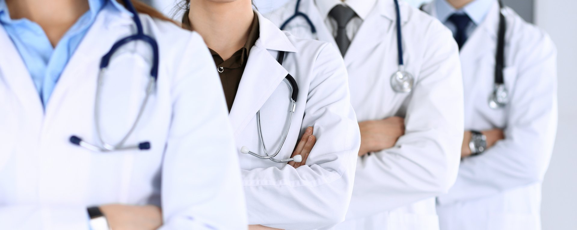 Eine Gruppe von modernen Doktoren steht als Team mit verschränkten Armen in einem Krankenhaus-Büro.