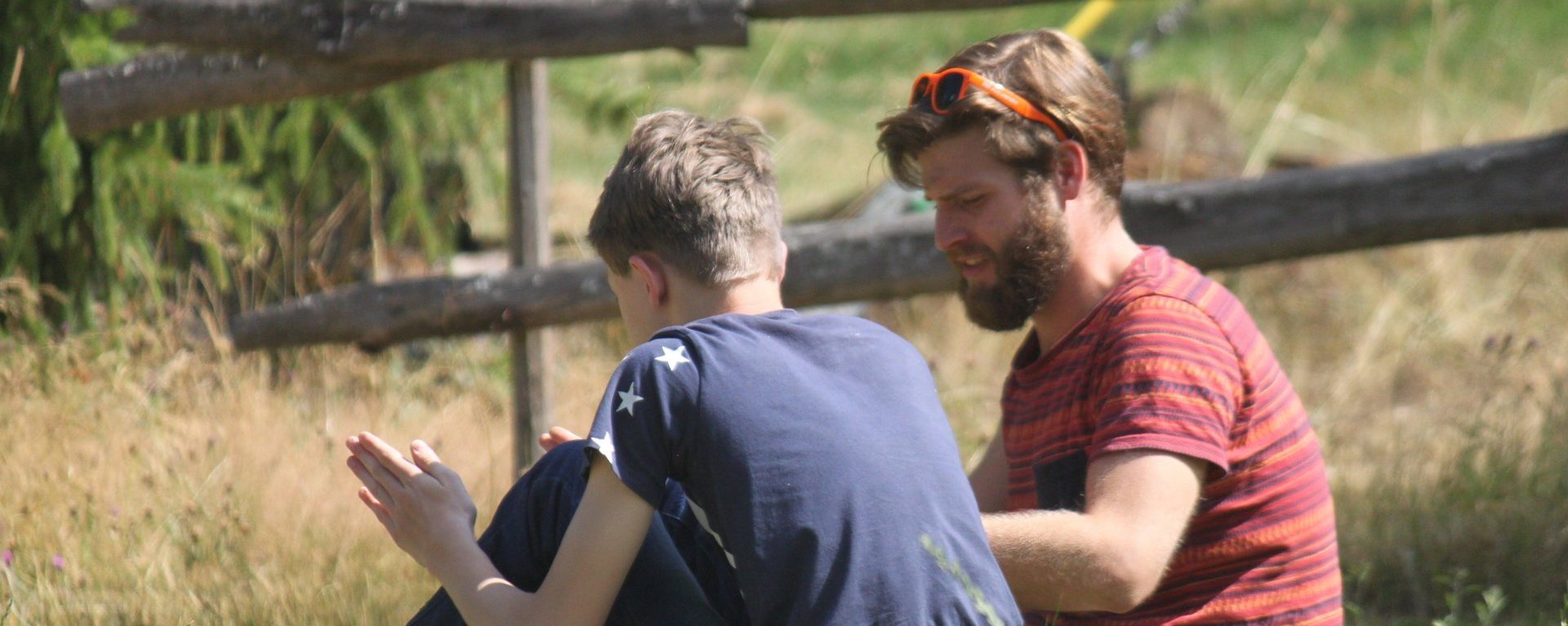 Ein Junge sitzt mit seinem Betreuer auf einer Wiese und unterhält sich mit ihm.