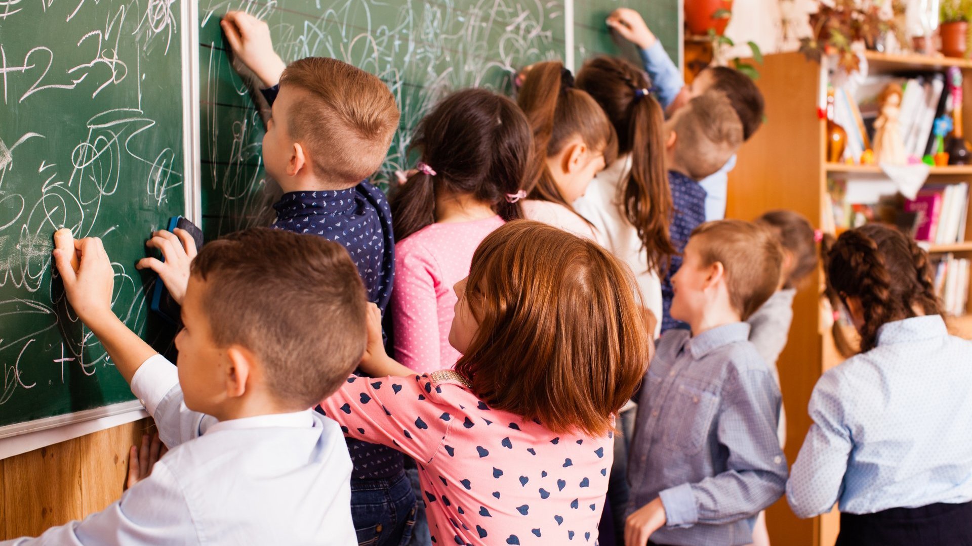 Einige Schülerinnen und Schüler malen etwas mit Kreide an eine grüne Schultafel.