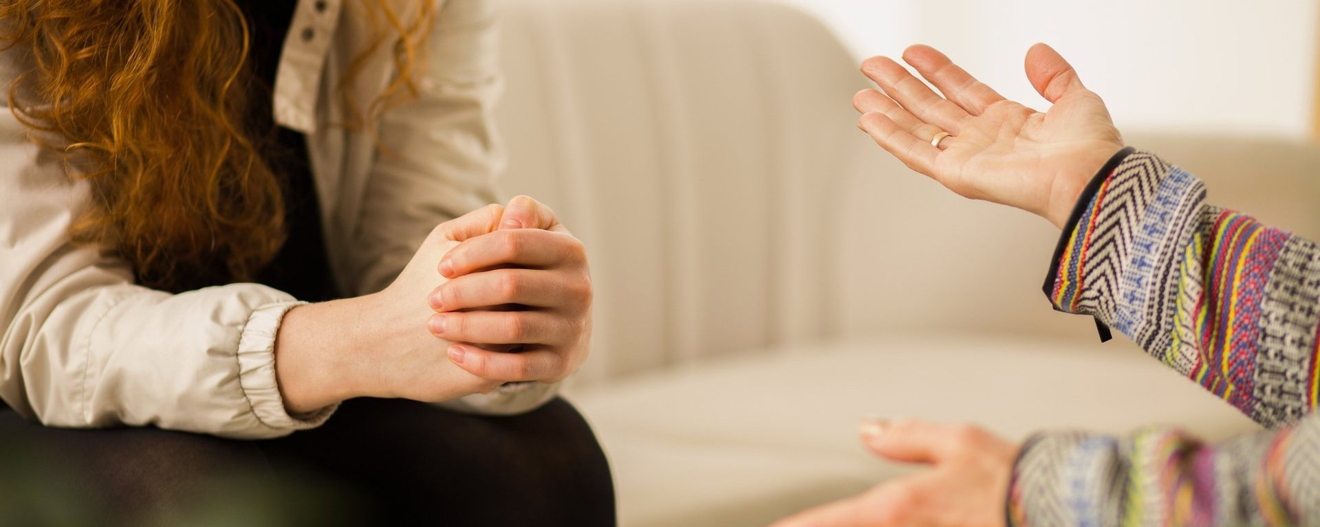 Nahaufnahme von einer Psychologin, die eine Frau berät. Eine der Frauen sitzt auf einem hellen Sofa.