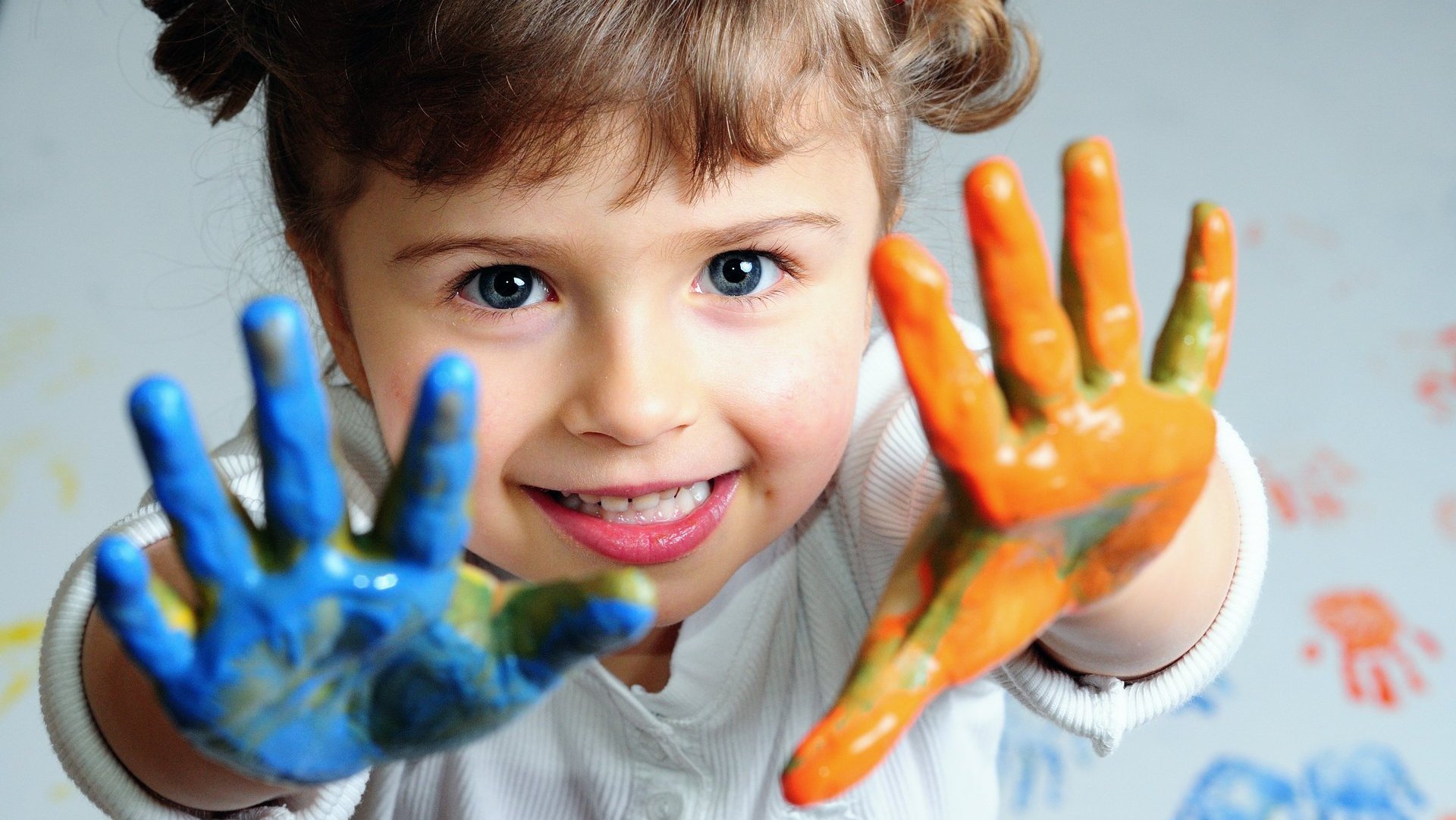 Kind mit Farbfingern Nahaufnahme eines Kindes mit einer blauen und orangen angemalten Hand.