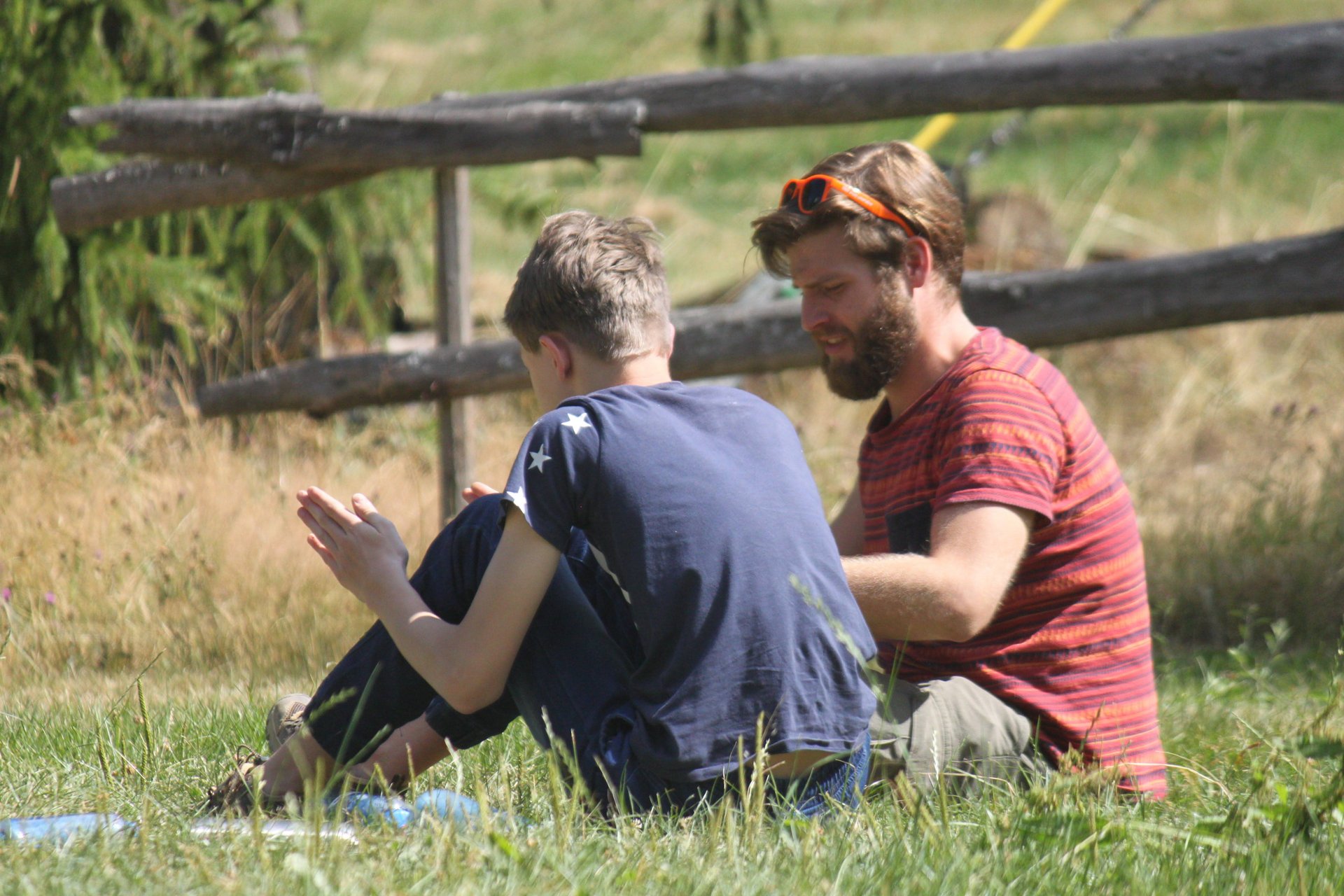 Ein Junge sitzt mit seinem Betreuer auf einer Wiese und unterhält sich mit ihm.